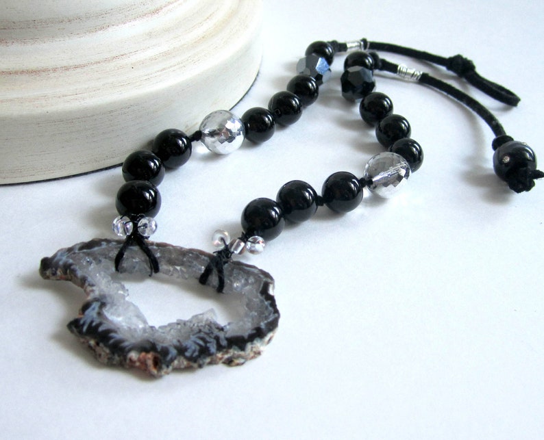 May include: A black and silver beaded necklace with a large, gray agate pendant. The pendant has a natural, rough-hewn edge and a hole in the center.
