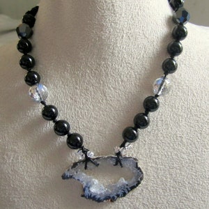 May include: A black beaded necklace with a crystal pendant featuring a large, natural agate slice with a white and gray interior.