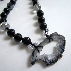 May include: A black and silver beaded necklace with a large, gray agate pendant. The pendant has a natural, rough-hewn shape with a hole in the center.
