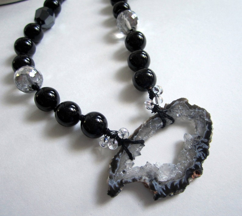 May include: A black and silver beaded necklace with a large, gray agate pendant. The pendant has a natural, rough-hewn shape with a hole in the center.