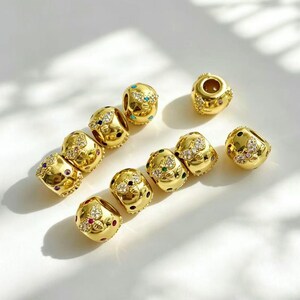 May include: A collection of gold-colored beads with intricate designs. Each bead is adorned with colorful gemstones and a butterfly motif. The beads are round and have a polished finish, reflecting light.