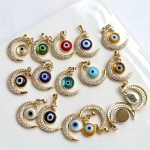 May include: Gold-toned crescent moon charms with various colored evil eye pendants. The charms are encrusted with small, clear crystals. The evil eye pendants feature colors like blue, green, red, and yellow.