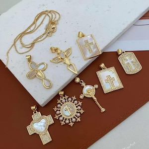 May include: A collection of gold-toned cross pendants with various designs, including crosses with pearl accents, heart shapes, and rectangular frames. Some pendants feature clear crystals. A gold chain is also present.