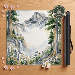 May include: A square playmat featuring a watercolor landscape of a mountain peak, pine trees, a waterfall, and wildflowers. A black cylindrical carrying case is positioned to the right. Two small white dice and two mahjong tiles are placed on the mat.