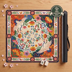 May include: A square game mat featuring a vibrant floral pattern with two white cranes, butterflies, and red berries. The mat has a dark blue border with circular flower motifs. Includes a black cylindrical carrying case and three mahjong tiles.