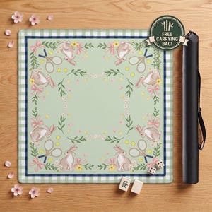 May include: A square light green game mat with a white and blue gingham border, featuring a repeating pattern of rabbits, tennis rackets, pink bows, and daisies. A black cylindrical carrying case and two white mahjong tiles are included.