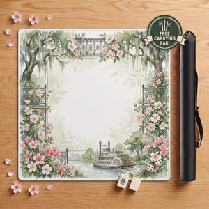 May include: A square game mat featuring a watercolour illustration of a riverboat on a waterway framed by pink flowers, green trees, and iron railings. The mat includes two white mahjong tiles and a black cylindrical carrying case with a circular label.