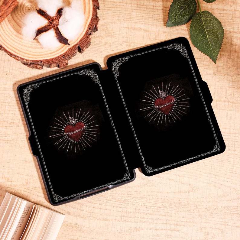 May include: Black tablet case with a decorative silver border. The case is open, revealing a red heart design with a crown and radiating lines on a black background. The design is centered within the case.