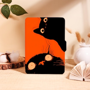 Può includere: Una custodia rettangolare per e-reader con uno sfondo arancione vibrante e due illustrazioni di gatti neri stilizzati. Un gatto è posizionato in alto e guarda verso il basso, mentre l'altro è in basso e guarda verso l'alto, entrambi con grandi occhi rotondi.