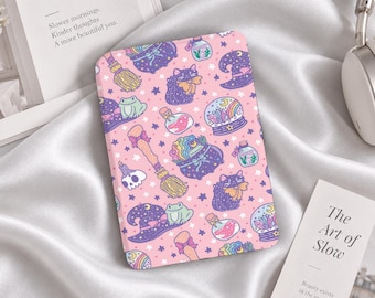 Könnte beinhalten: Eine rechteckige E-Reader-Hülle mit hellrosa Hintergrund und einem wiederkehrenden Muster aus violetten Hexenhüten, schwarzen Katzen, grünen Fröschen, Kristallkugeln, Zaubertrankflaschen, Totenköpfen und Besen, verziert mit kleinen violetten Sternen.