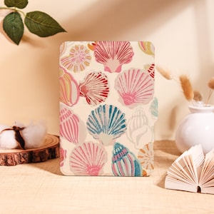 May include: A rectangular case featuring a seashell pattern in shades of pink, red, blue, and cream. The design includes various seashell illustrations. The case is standing upright on a light-colored surface.