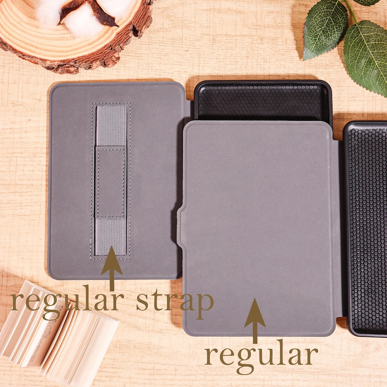May include: Gray tablet cases with the text "regular strap" and "regular". One case is open, revealing a black interior. The cases are on a wooden surface, with a piece of wood and leaves in the background.