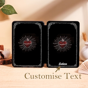 May include: Black case with a red heart design, radiating light, and a decorative border. The text "Sakura" is printed on the bottom right. The words "Customise Text" are printed at the bottom.