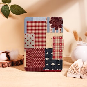 May include: A tablet case with a patchwork design, incorporating red plaid, heart motifs, and floral patterns. The case includes a magnetic closure and a dark red flower embellishment. The colour palette is a blend of red, cream, and blue.