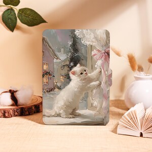 Può includere: Custodia per tablet con dipinto di un gattino bianco che raggiunge un nastro rosa. L'opera raffigura una scena invernale innevata con una casa e tende di pizzo. La custodia è progettata per proteggere un tablet.