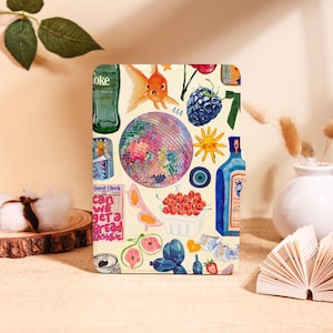 May include: A rectangular, cream-colored notebook with a collage of colorful illustrations. The design includes a disco ball, goldfish, berries, a bottle of gin, and the text "Can we get a bread basket?"
