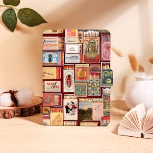 Może przedstawiać: Prostokątne etui z kolażem wzorów zapałek w stylu vintage na czerwonym tle. Zapałki zawierają różne grafiki i teksty, w tym "Janeo Safety Matches" i "New Desa". Etui jest prawdopodobnie przeznaczone na tablet lub czytnik e-booków.