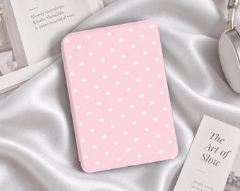 Könnte beinhalten: Ein rechteckiges E-Reader-Gerät mit einer hellrosa Hülle und einem wiederkehrenden Muster aus kleinen weißen Punkten. Das Gerät ist mittig platziert, umgeben von weißem Satinstoff, einem Buch mit dem Text Quiet Life und einem Kopfhörer.