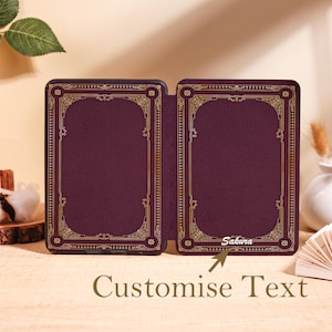 Puede incluir: Una funda de lector electr&oacute;nico burdeos con un dise&ntilde;o de borde dorado ornamentado. La funda est&aacute; abierta, revelando el interior. El texto "Sakura" es visible en el lado derecho. Las palabras "Customise Text" est&aacute;n en la parte inferior.