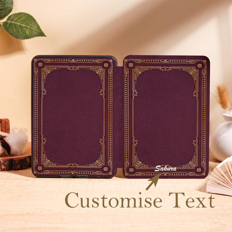 Puede incluir: Una funda de lector electr&oacute;nico burdeos con un dise&ntilde;o de borde dorado ornamentado. La funda est&aacute; abierta, revelando el interior. El texto "Sakura" es visible en el lado derecho. Las palabras "Customise Text" est&aacute;n en la parte inferior.