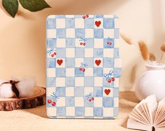 May include: A rectangular e-reader case featuring a light blue and white checkered pattern. The design is decorated with small red hearts and pairs of red cherries tied with blue ribbons scattered across the surface of the cover.
