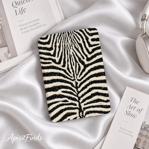 May include: A rectangular e-reader cover featuring a black and white zebra stripe pattern. The cover is positioned centrally, displaying a symmetrical arrangement of dark stripes against a light background, with rounded corners and a smooth texture.