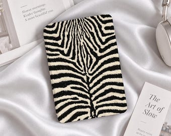 Puede incluir: Una funda rectangular para lector electrónico con un patrón de rayas de cebra en blanco y negro. La funda está colocada en el centro, mostrando una disposición simétrica de rayas oscuras sobre un fondo claro, con esquinas redondeadas y textura lisa.