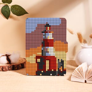 May include: A rectangular e-reader cover featuring a pixel art design of a lighthouse. The lighthouse is rendered in shades of red, white, and dark gray against a background of orange, brown, and light blue squares, creating a grid-like mosaic.