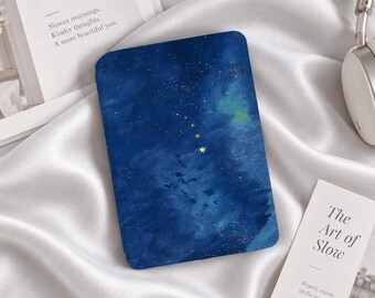 Könnte beinhalten: Eine rechteckige E-Reader-Hülle mit einem dunkelblauen Nachthimmel-Design im Aquarellstil, das mit weißen Sternen und drei markanten, goldfarbenen Sternsymbolen in der Mitte des Covers versehen ist.
