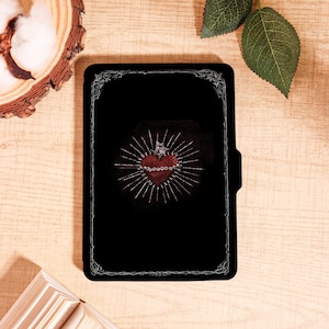 May include: Black tablet case featuring a red heart design with a crown and radiating lines. The heart is surrounded by a silver-colored border. The case has a magnetic closure and a decorative silver border.