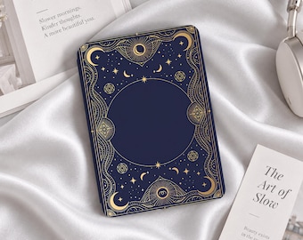 May include: A rectangular e-reader case featuring a dark navy blue background with intricate gold celestial patterns, including crescent moons, stars, and geometric circular motifs surrounding a large, solid navy blue central circle.