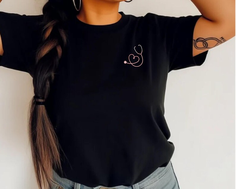 May include: Black t-shirt with a pink stethoscope design on the front. The stethoscope is shaped like a heart.
