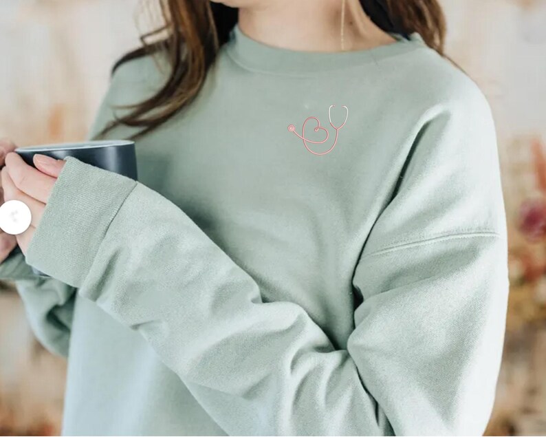 May include: A light green sweatshirt with a pink and white heart and stethoscope design on the front.