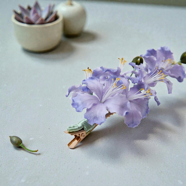 Macro detail of purple Ronghua flower showing fuzzy silk texture and yellow stamens. Hand-trimmed velvet sculpture hair clip resting on a surface. Traditional Chinese floral art.