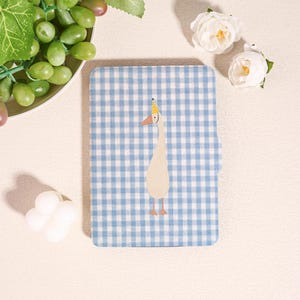 May include: A blue and white checkered notebook featuring a whimsical illustration of a goose wearing a party hat. The notebook is rectangular and has a light blue and white gingham pattern. The goose is cream-colored with orange feet and beak.