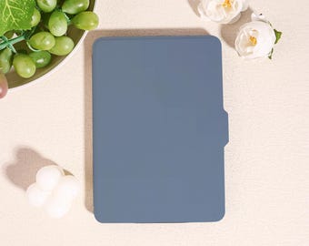 May include: A slate blue tablet case with a side tab, set on a cream-coloured surface. The case is rectangular with rounded corners. Grapes and white roses are arranged around the case.