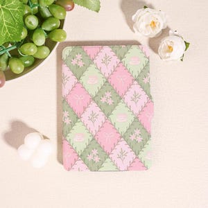 May include: A rectangular notebook with a pink, green, and white quilted pattern. The pattern includes teacups, bows, and floral designs. The notebook is surrounded by white flowers and grapes.