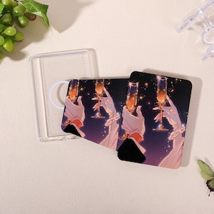 Pode incluir: Duas capas de telefone retangulares com um desenho de uma mão enluvada segurando uma taça de champanhe. O desenho apresenta um fundo escuro com estrelas brilhantes. Uma capa de telefone transparente também é visível.