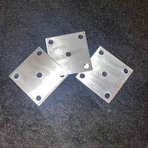 May include: Three silver metal square plates with rounded corners and four holes each. The plates are arranged in a triangular shape.