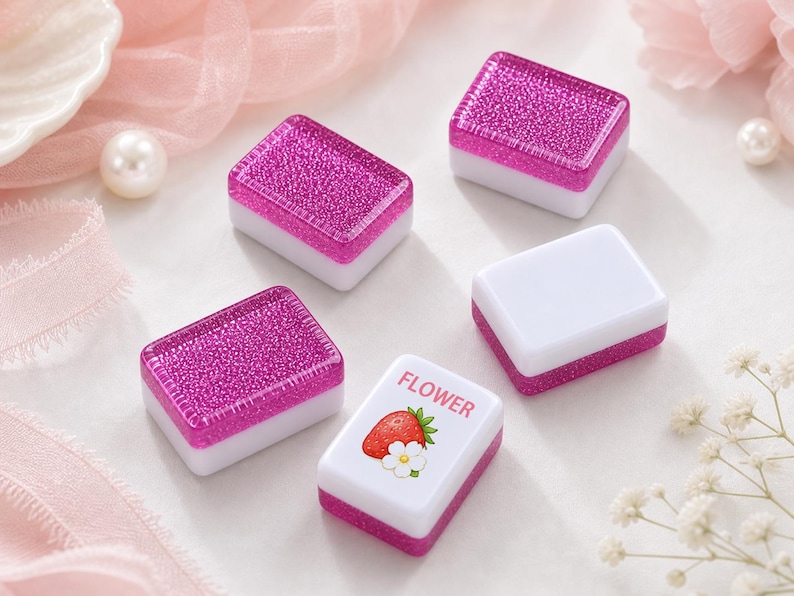 May include: Five rectangular mahjong tiles with a two-tone design. Four tiles feature a solid white base with a vibrant, glittery magenta top. One tile has a white base with a magenta bottom and a graphic of a red strawberry and white flower with the text FLOWER.