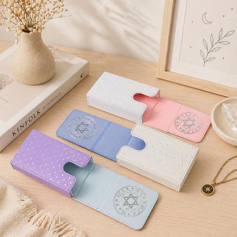 May include: Four open card cases in white, pink, light blue, and purple, each with a matching interior and a silver Star of David design. The cases are on a light wood surface, with a vase of flowers and a framed illustration in the background.