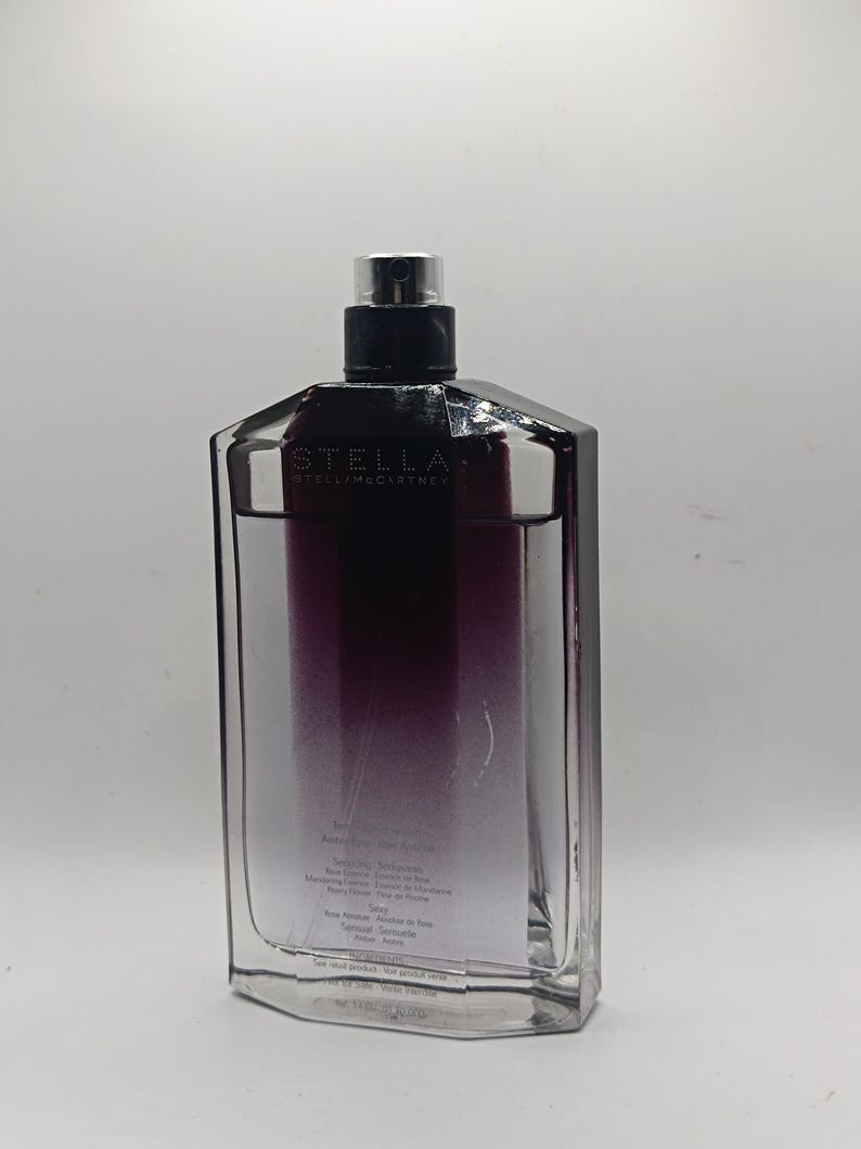 May include: A rectangular perfume bottle with a black cap and a gradient of purple to clear liquid. The bottle has the brand name "STELLA" printed on the front.