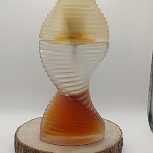 Op de afbeelding: Een glazen parfumfles met een gedraaid, geribbeld ontwerp dat overgaat van een helder, mat bovendeel naar een warme, amberkleurige basis. De fles heeft een afgeronde, getrapte dop die past bij de horizontale, geribbelde textuur van het lichaam.