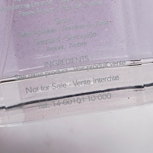May include: A clear, rectangular container with text in English and French. The text includes "Seducing," "Rose Essence," and "Sexy." The container also has the text "Not for Sale."