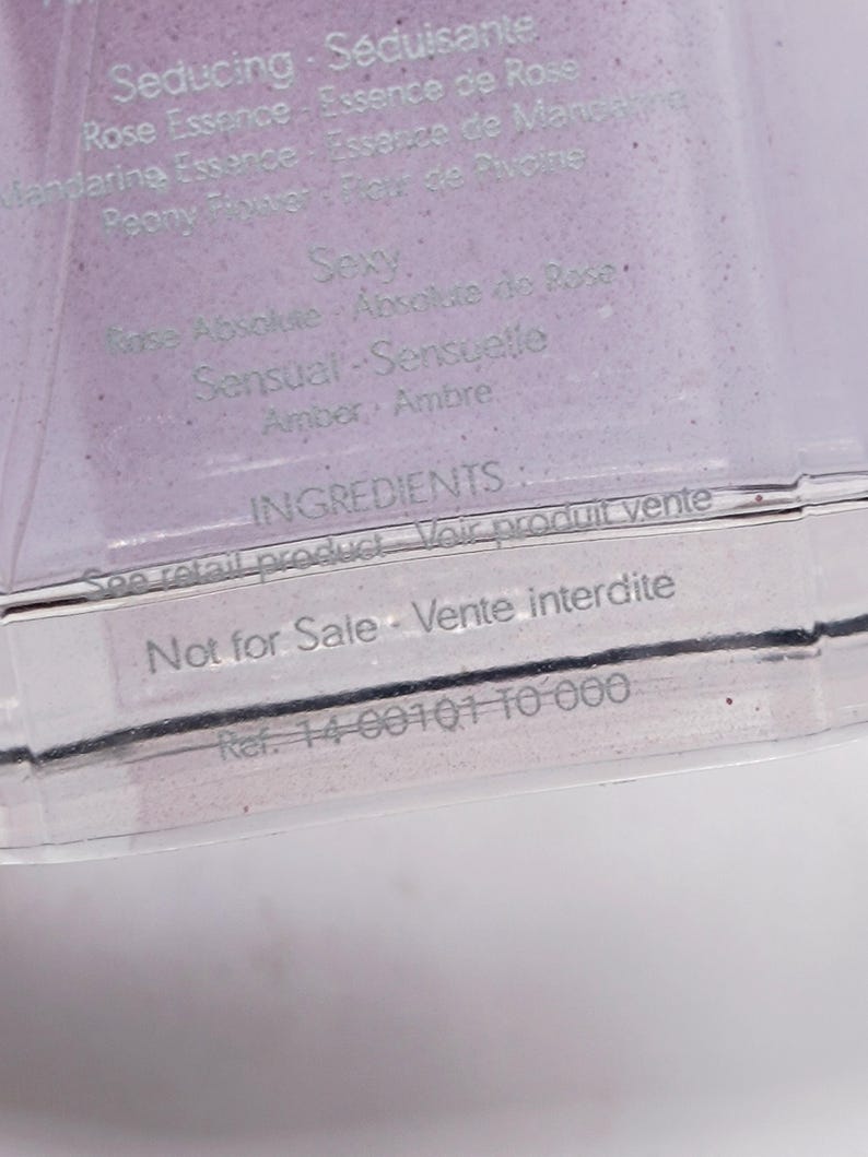 May include: A clear, rectangular container with text in English and French. The text includes "Seducing," "Rose Essence," and "Sexy." The container also has the text "Not for Sale."