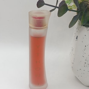 Puede incluir: Un frasco de perfume de vidrio esmerilado con tapón transparente. La botella está llena de un líquido rojo-anaranjado y tiene la palabra "PYTHON" impresa verticalmente. La marca "TRUSSARDI" está impresa en la parte inferior.