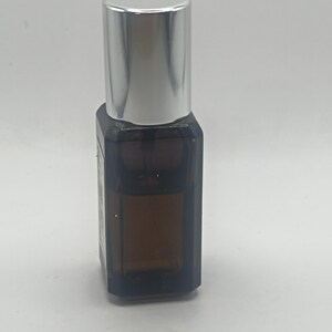 May include: A small, brown glass bottle with a silver cap. The bottle has a rectangular shape and appears to contain a liquid. The cap is cylindrical and shiny. The bottle is set against a plain white background.