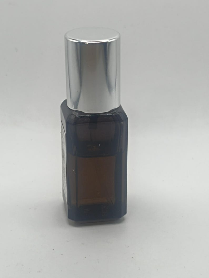 May include: A small, brown glass bottle with a silver cap. The bottle has a rectangular shape and appears to contain a liquid. The cap is cylindrical and shiny. The bottle is set against a plain white background.