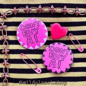 May include: A collection of punk-inspired accessories, including two pink buttons with the text "DON'T BUY A.I.", two pink safety pins, and a pink heart-shaped charm. A spiked chain is at the top and left. The background is yellow and black striped.