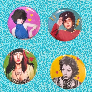 May include: Four round button pins featuring colorful illustrations of women with different hairstyles and clothing. The pins have a white background with yellow lightning bolts and hearts.